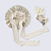 A beige silk sleep bonnet with a gathered top and long ties, next to a small bowl of white hair accessories.