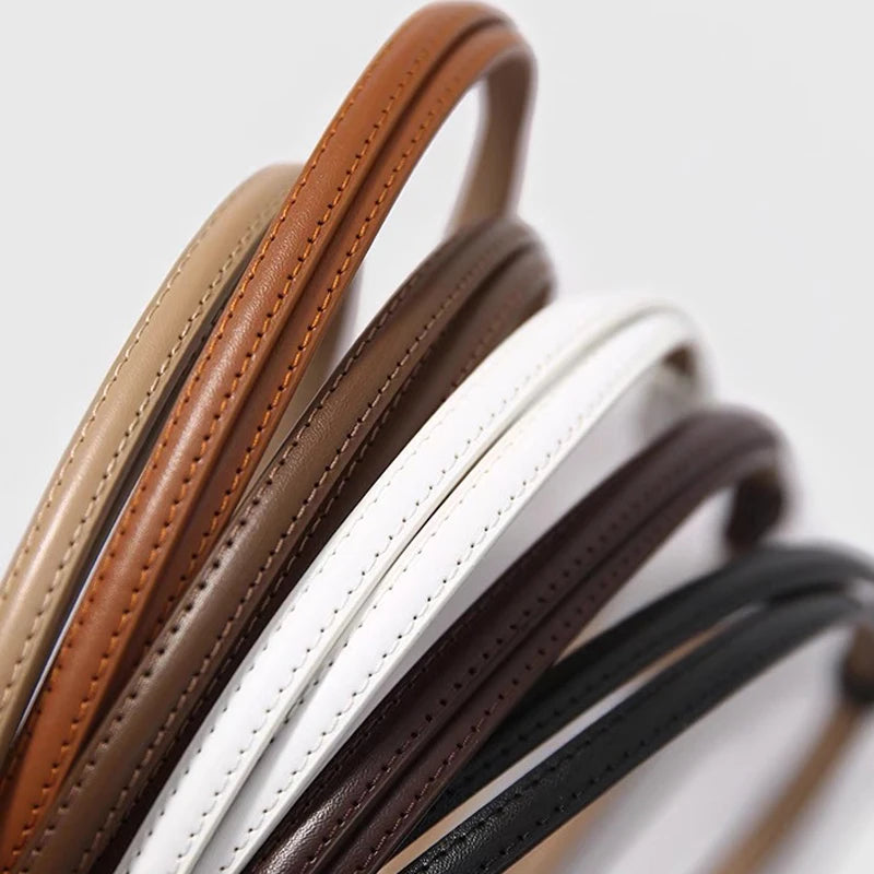 A close-up of several skinny leather belts in various shades including brown, tan, black, and white.