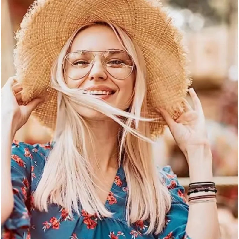 A blonde woman wearing a straw hat and glasses smiles while holding her hair, suggesting boho hair ties or headbands.