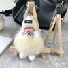 A white knitted plush doll with a pink face and a black bow is displayed on a wooden hanger.