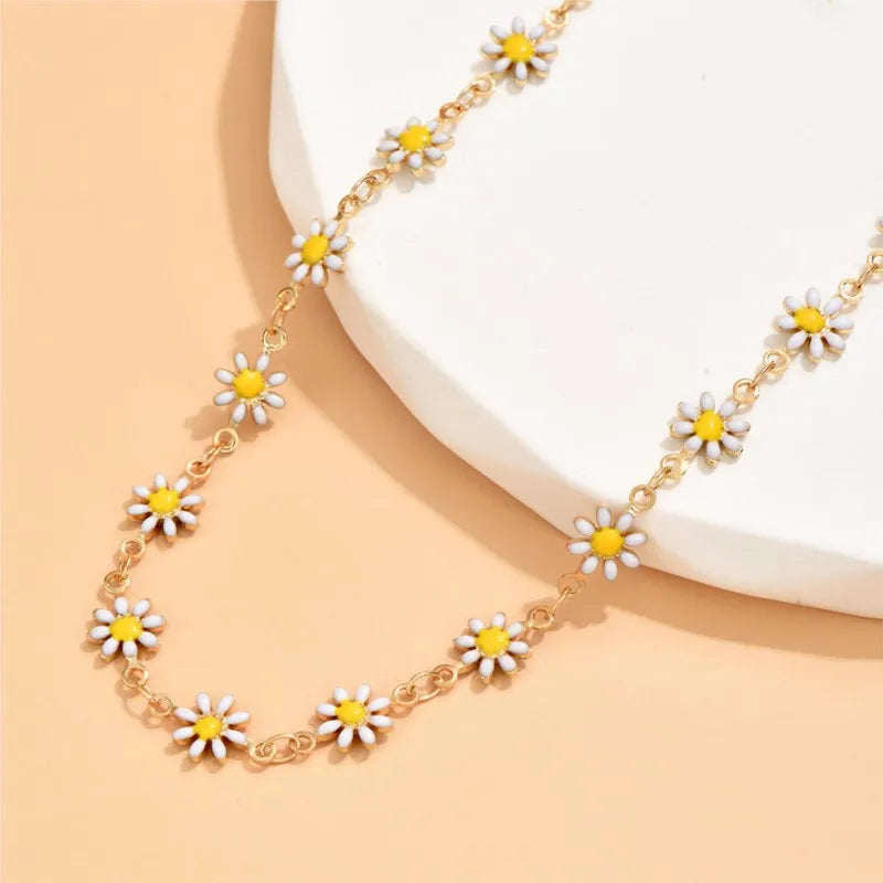 Gold enamel daisy chain anklet with white and yellow flowers displayed on a light background.