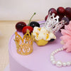 Gold and silver mini crown cake toppers displayed on a purple cake with red and black berries.