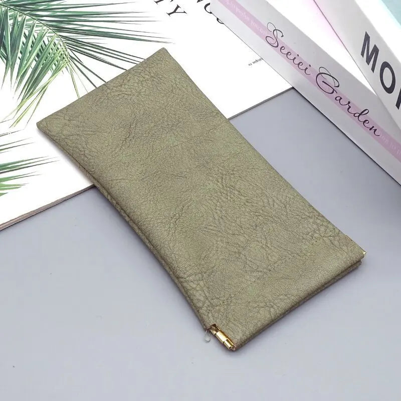 A rectangular, light olive green PU leather storage bag lying on a gray surface next to a book.