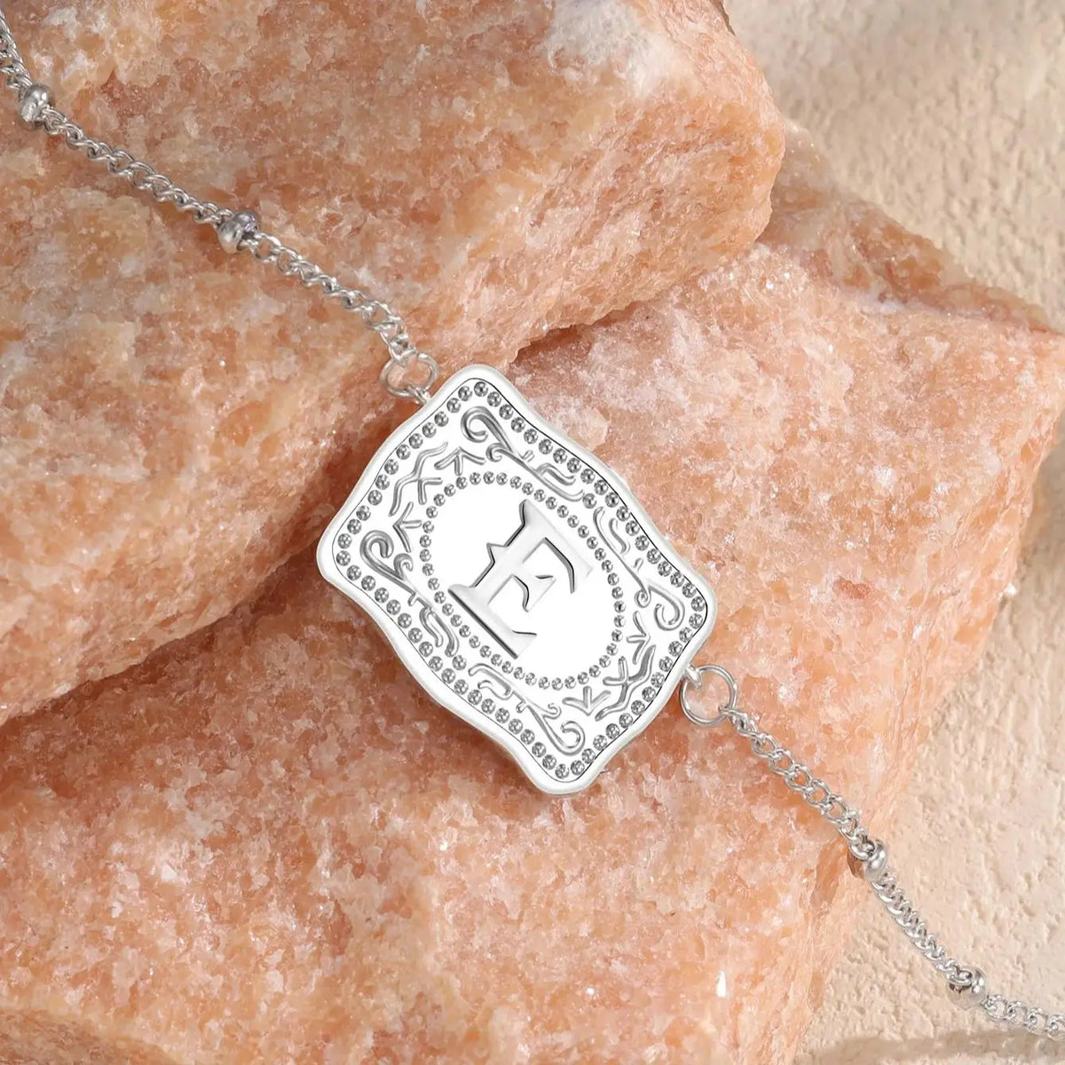 Silver initial letter pendant necklace with an engraved E resting on a pink crystal stone.