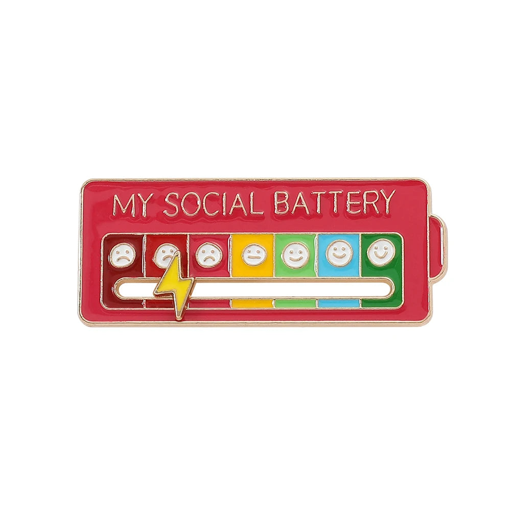 A red brooch pin labeled MY SOCIAL BATTERY featuring multiple small facial expressions.