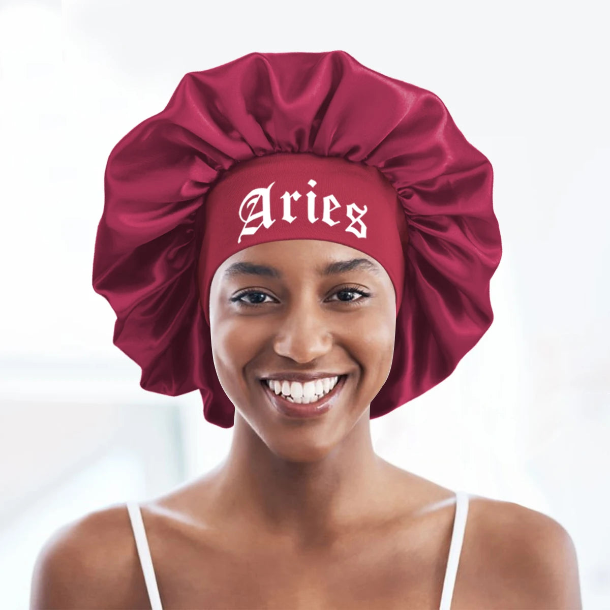 A smiling woman wearing a deep red satin sleep bonnet with an Aries wrap band.