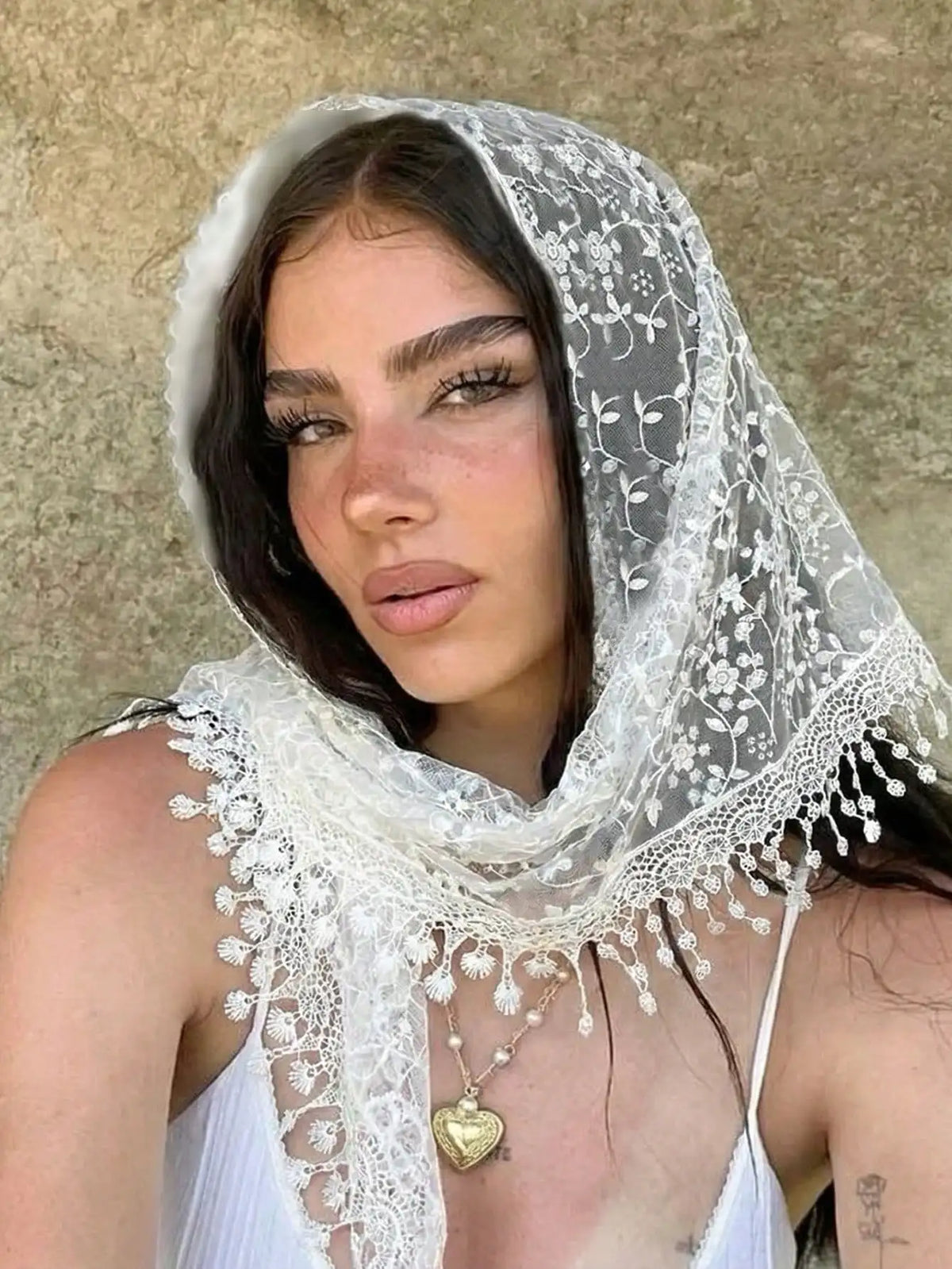 A woman wearing a sheer white floral lace scarf and headscarf set against a neutral background.