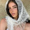 A woman wearing a sheer white floral lace scarf and headscarf set against a neutral background.