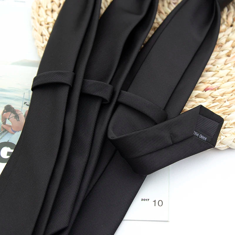 A close-up of solid black neckties folded and displayed on a woven natural fiber background.