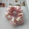 Gomas para el cabello de seda morada rosa con estampado floral sobre fondo blanco.