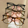 A hand holds a set of three classic square anti-blue light eyeglasses in brown, olive green, and leopard print patterns.