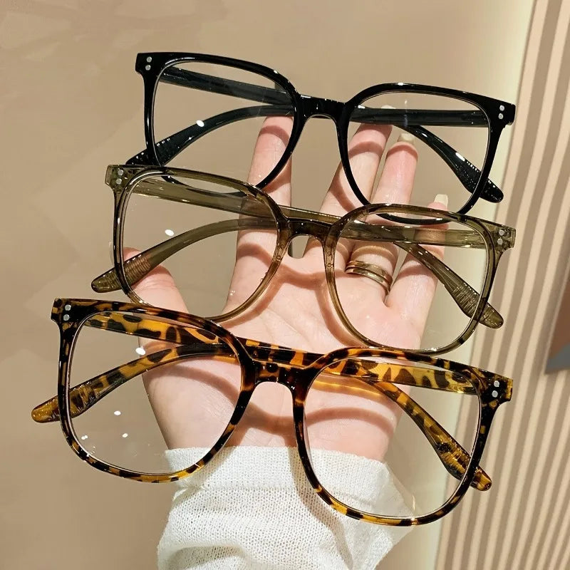 A hand holds a set of three classic square anti-blue light eyeglasses in brown, olive green, and leopard print patterns.