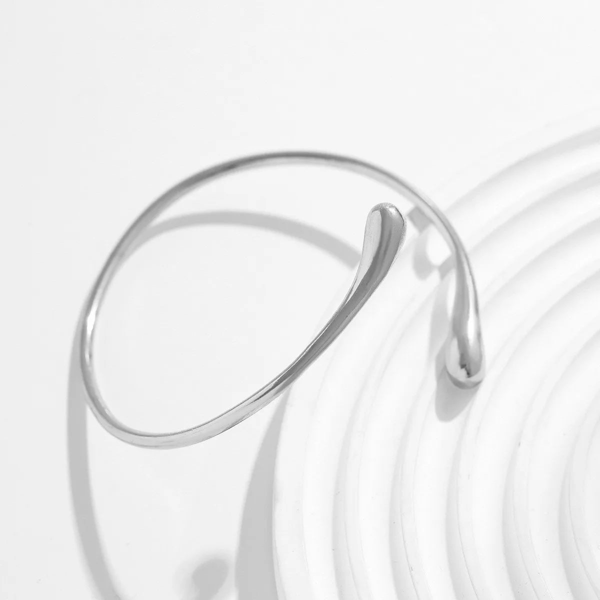 A close-up of a silver gold droplet arm bangle with an adjustable design, shown against a bright white background.