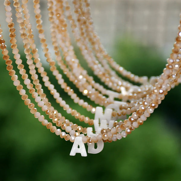 A close-up of a delicate necklace featuring mother of pearl beads and crystal accents, with a white initial charm.