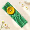 A green plaid fabric headband with a yellow polka dot button attached, surrounded by white daisies.