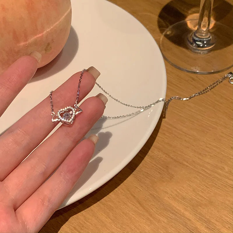 A hand holds a pink crystal heart necklace resting on a white plate.