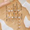 A collection of gold dangle curved belly piercing jewelry featuring heart and flower designs displayed on a beige background.