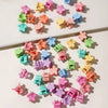A collection of colorful mini flower hair clips in shades of pink, purple, green, and blue scattered on a white surface.