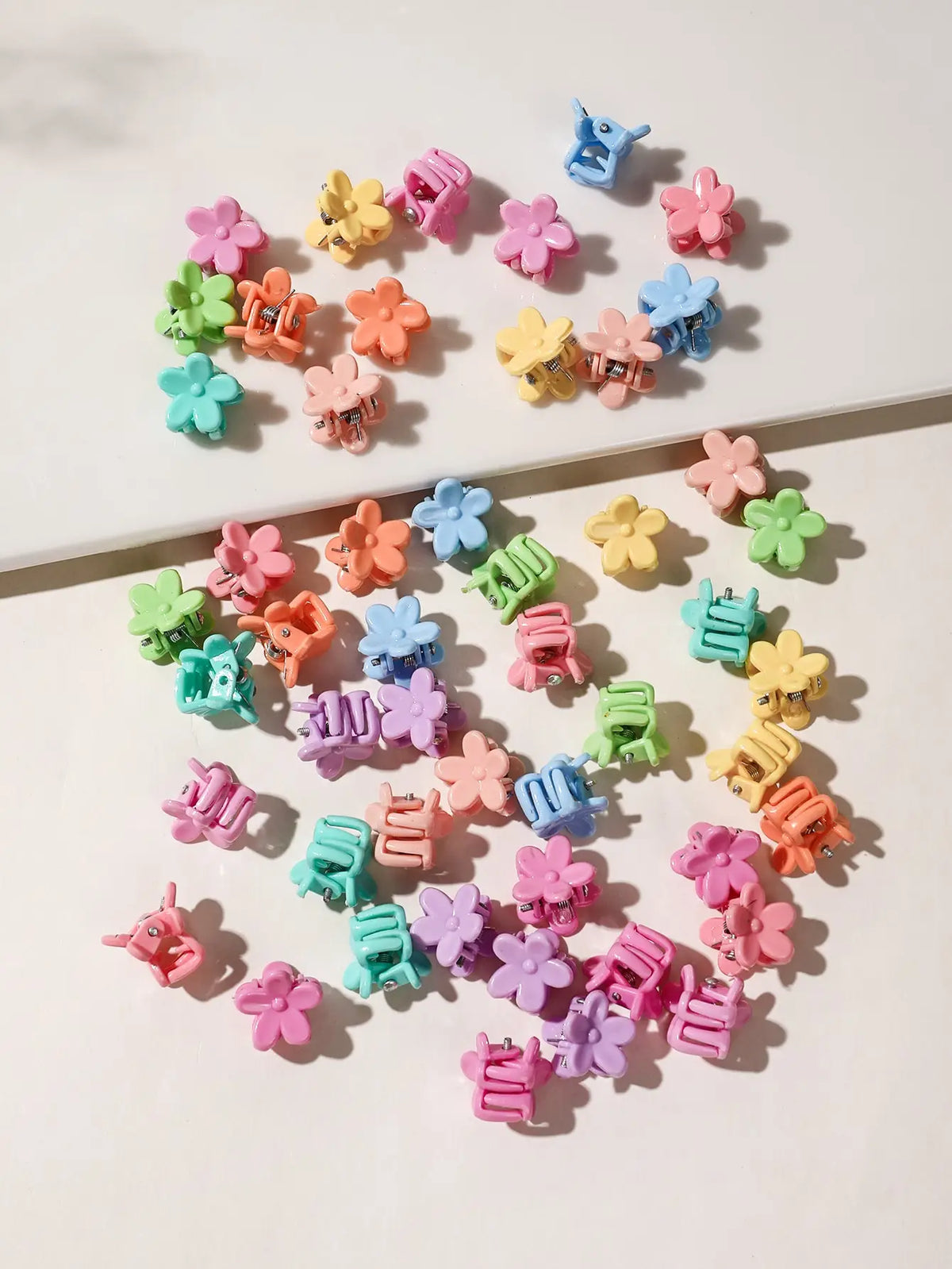 A collection of colorful mini flower hair clips in shades of pink, purple, green, and blue scattered on a white surface.
