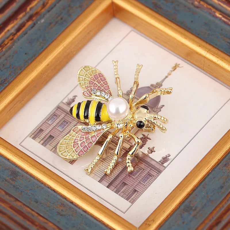 Broche dorée avec motif d'abeille aux rayures jaunes et noires et un centre de perle, dans un cadre en bois.