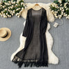 Black knitted shawl cardigan with mesh detailing draped over a white fluffy rug surrounded by white flowers