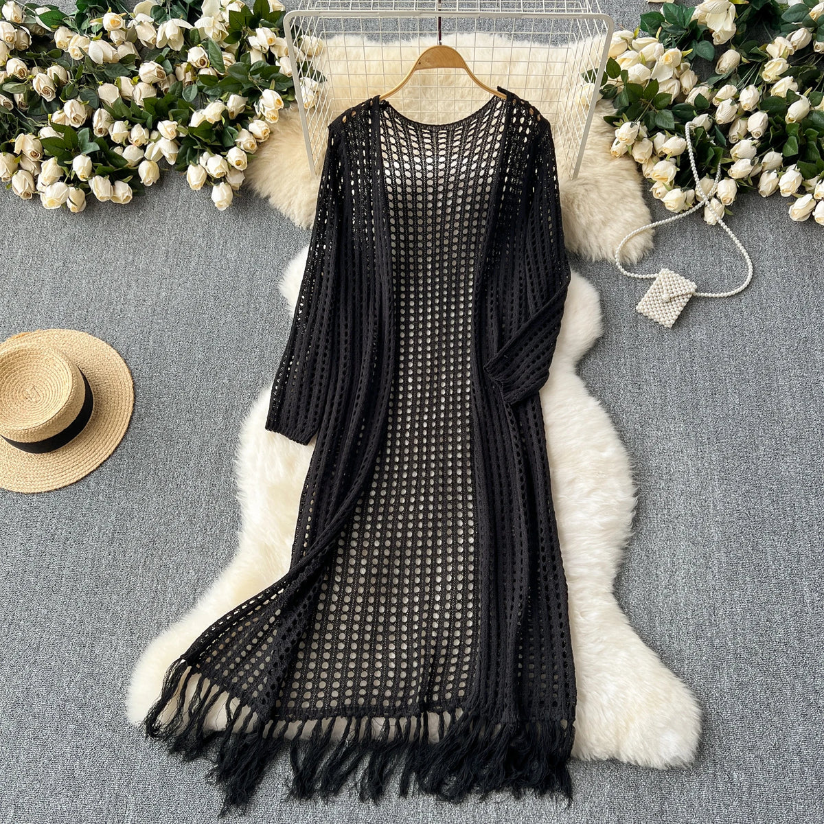 Black knitted shawl cardigan with mesh detailing draped over a white fluffy rug surrounded by white flowers