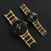 A pair of gold-toned analog quartz watches with black dials and straps resting on a dark surface.