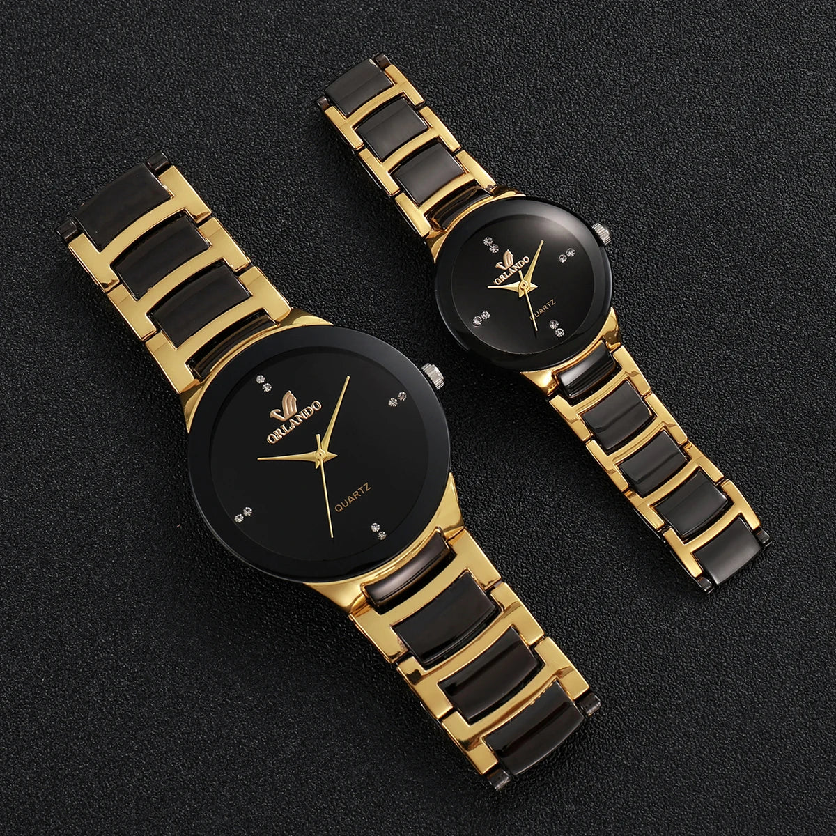 A pair of gold-toned analog quartz watches with black dials and straps resting on a dark surface.