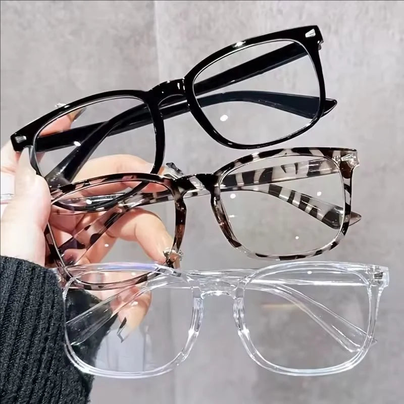 Une main tient des lunettes transparentes bleues minimalistes avec des montures noires.