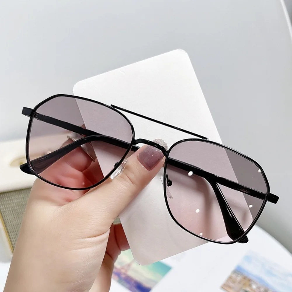 A hand holds a pair of classic metal frame square sunglasses with tinted lenses against a white background.