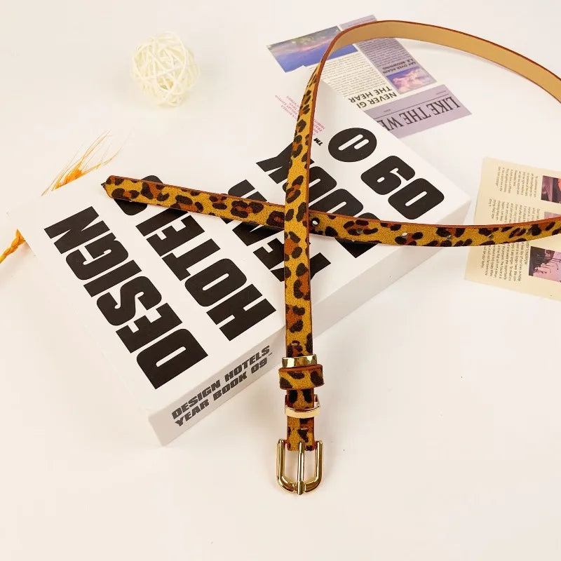 A slim brown leopard print PU leather belt with a vintage gold buckle resting on a white background.