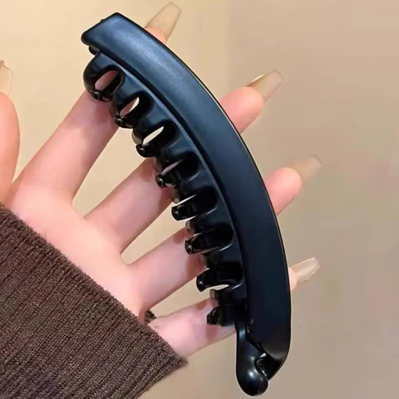 Eine Hand hält eine schwarze, gebogene Haarnadel oder Haarnadel mit mehreren kleinen Zinken.