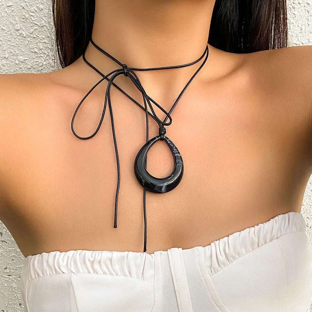 A black rope choker necklace with a circular pendant worn by a woman.