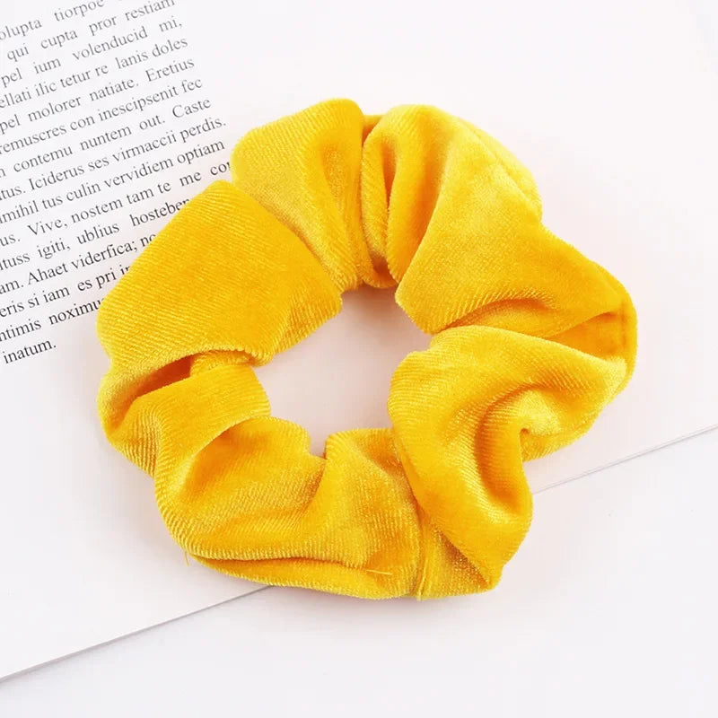 A set of six yellow velvet scrunchies for hair ties displayed on a white background.