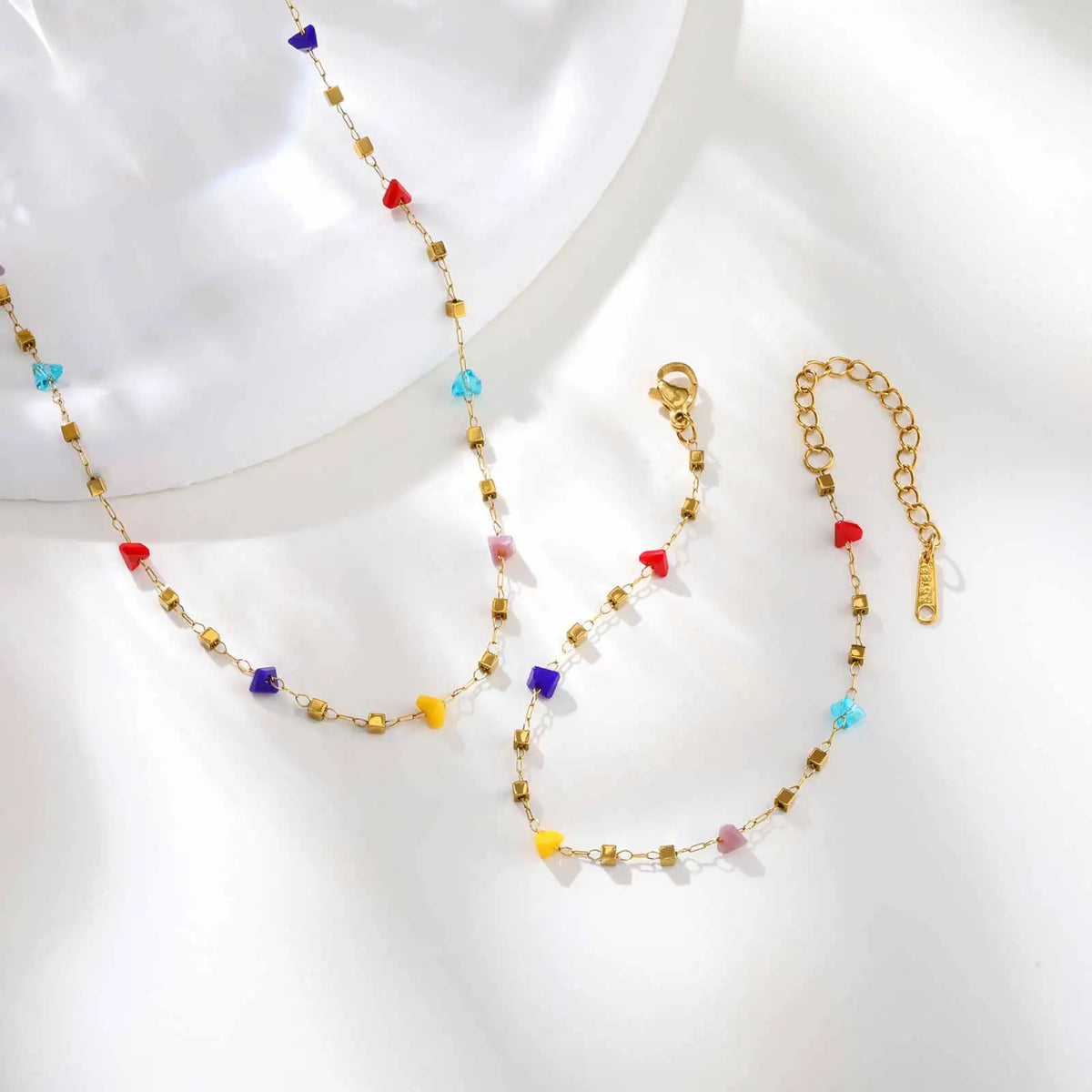 A delicate gold chain necklace featuring irregular colored gemstone beads in red, blue, purple, and yellow.