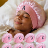 A set of pink A-Z letter sleep caps for kids laid out on a white sheet.