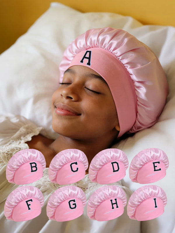 A set of pink A-Z letter sleep caps for kids laid out on a white sheet.