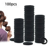 A stack of black seamless elastic hair ties and a single black rubber band are shown next to a person's hair.
