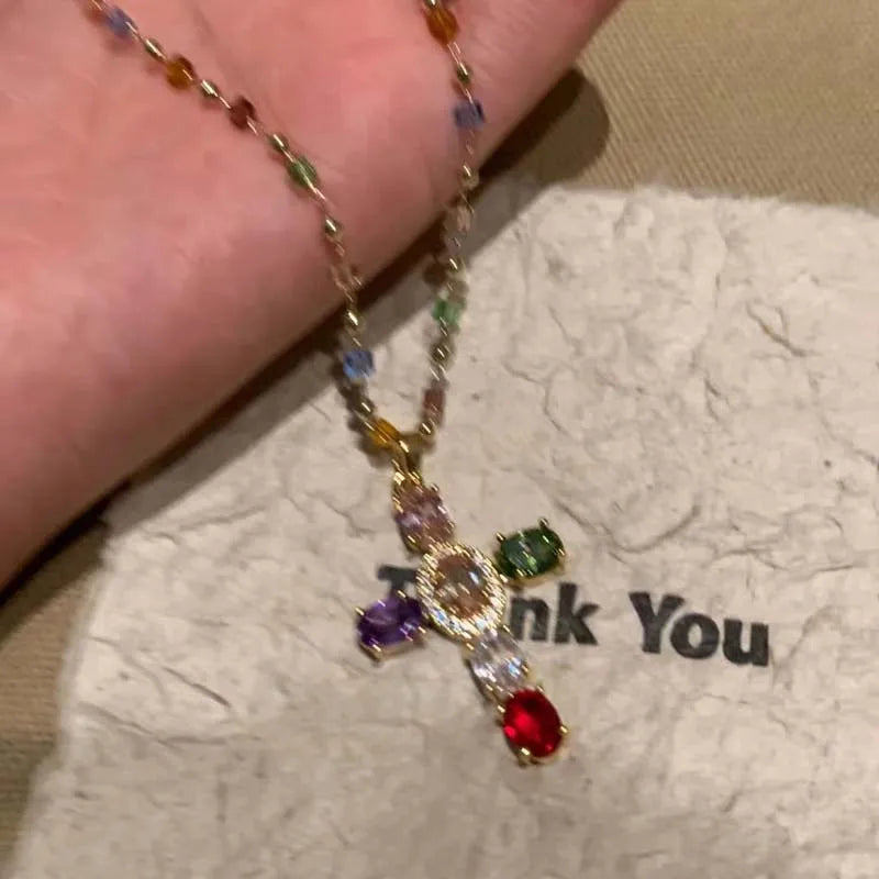 A colorful zircon cross pendant necklace with various colored stones on a delicate chain.