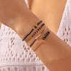 A close-up of a wrist displaying a stack of bohemian pearl beaded bracelets in black and gold tones.