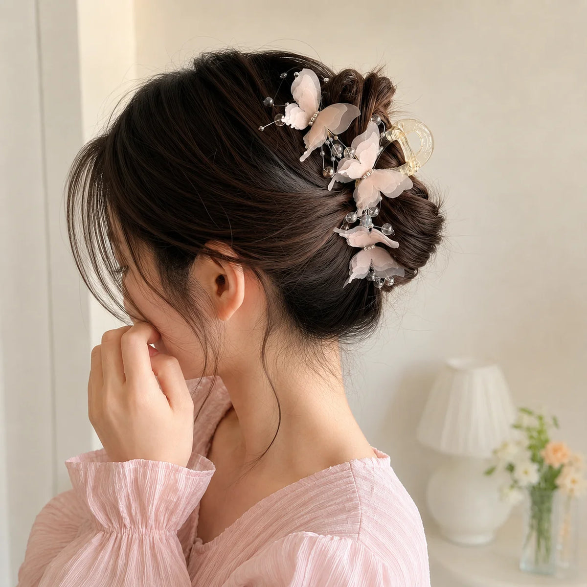 A woman with dark hair is shown in a side profile wearing a pink blouse and a pearl rhinestone butterfly hair claw clip in he