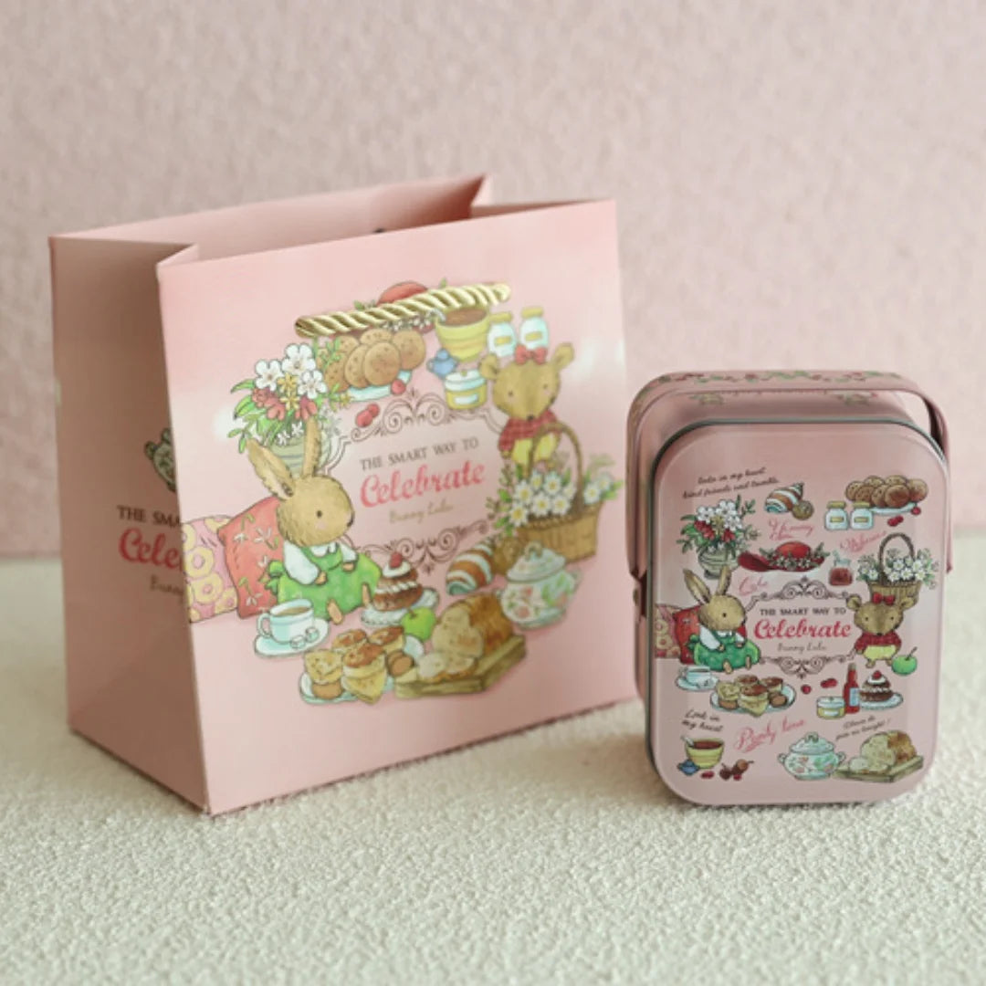 A pink decorative tinplate candy box with a carrying loop featuring illustrations of treats and animals.