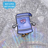 A purple cartoon enamel pin shaped like a shirt with blue stripes is displayed on a clear, textured surface.