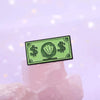 A green enamel dollar banknote brooch featuring an ocean shell charm resting on pink quartz.