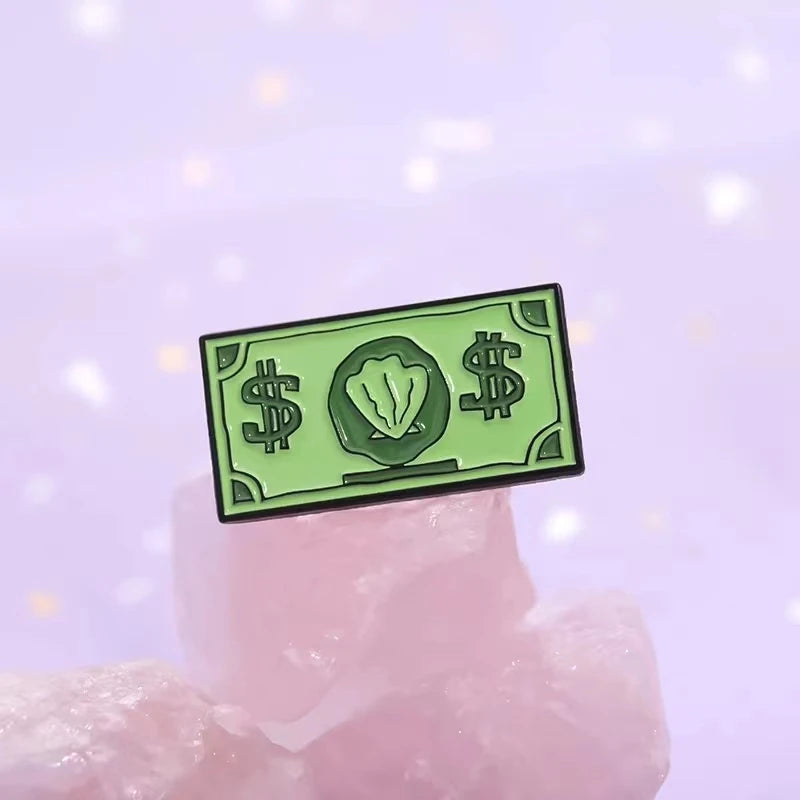 A green enamel dollar banknote brooch featuring an ocean shell charm resting on pink quartz.