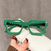 A pair of square green anti-blue light computer glasses resting on a white object.