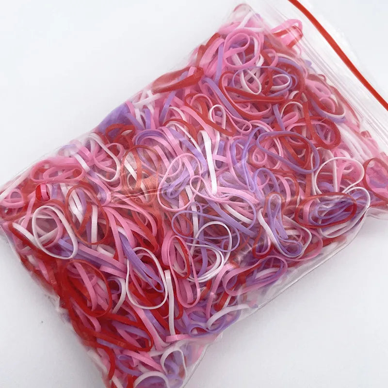 A clear plastic bag filled with colorful disposable hair scrunchies in shades of pink and purple.