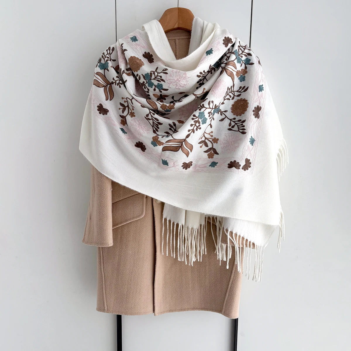 A beige luxury floral scarf with muted pink and green botanical patterns draped over a light pink coat.