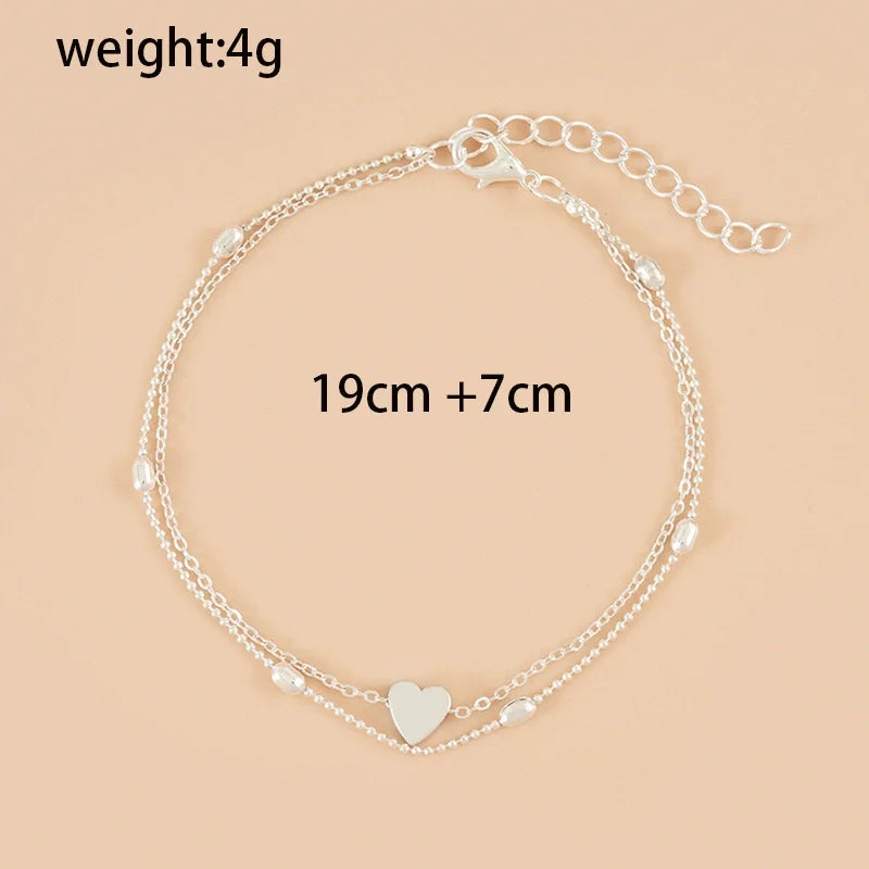 Sandale à bracelets argentés avec un charm en forme de cœur, présentée sur fond neutre.