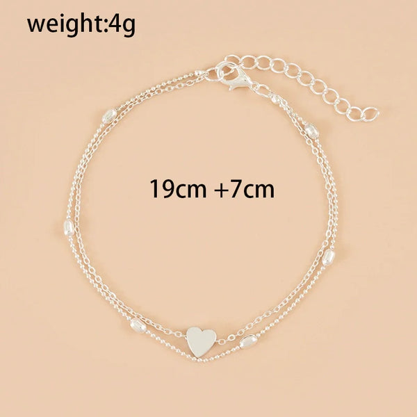 Sandale à bracelets argentés avec un charm en forme de cœur, présentée sur fond neutre.